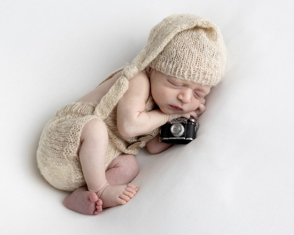 Creative newborn portrait featuring a baby posed with a camera prop photographed in my Boston Metrowest studio.