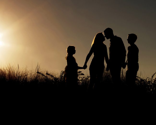 Silhouette family portrait photographed on the beach at sunset by Paula Swift Photography