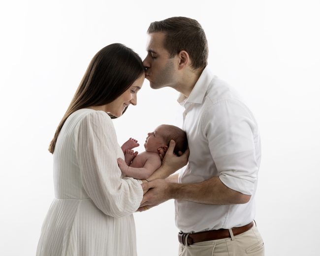 Boston Metrowest newborn and family photographer capturing parents holding their newborn in a studio portrait